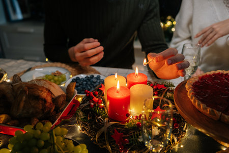 Close-up cropped shot of unrecognizable man using match lighting candles sitting at holiday table with loving family in dark living room with cozy interior, on Christmas eve, home festive atmosphere.の写真素材