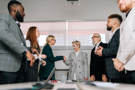 Low-angle view of middle-aged businesswoman handshaking female partner at group meeting making business agreement contract deal, concluding trust partnership contract after negotiations.の写真素材
