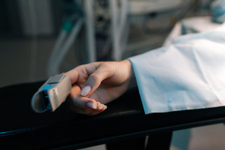 Closeup cropped shot of unrecognizable female hand with pulse oximeter on finger on operating table under anesthesia operating room. Process of medical surgery. Concept of surgery and emergency.の写真素材