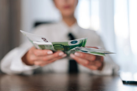 Closeup selective focus of successful business woman holding pack of hundred-euro bills and counts them. Concept of wealth, inflation, internet business, family budget, online trading and e-commerce.の写真素材