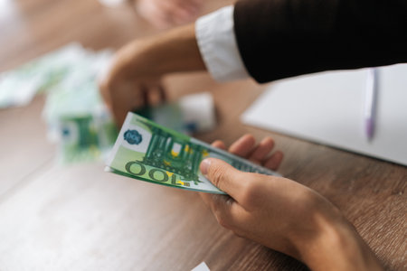 Close-up cropped shot of unrecognizable businessman in suit counting money at workplace sitting at desk. Successful business man rejoicing good deal. Male manager counting paper euro.の写真素材