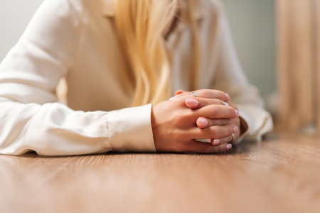 Closeup cropped shot of unrecognizable woman sitting at desk with folded arms. Close-up of concentrated businesswoman during business consultation in office. Corporate woman in posing at workplace.の写真素材