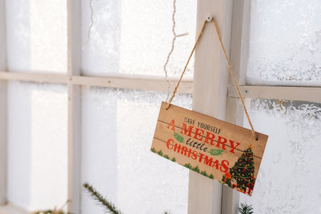 Merry Christmas sign on wall with frozen window on sunny day. Closeup of sign on door at Christmas display in home. Christmas decorations, preparing for festive season.の写真素材