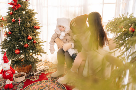 Remote view of happy family wearing winter clothes sitting in decorated room of summer house on Christmas eve. Young mother and father with loving child baby having fun. Family gathering together.の写真素材