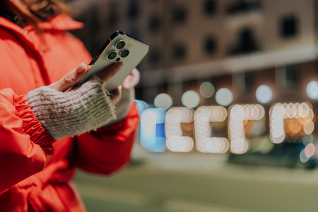 Closeup hands of unrecognizable woman typing on mobile phone at dark night city street on blurred...