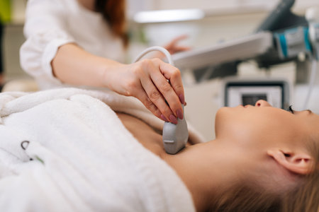 Closeup of beautiful woman examine thyroid gland with ultrasound probe in medical clinic. Close-up of unrecognizable female doctor holding ultrasound probe along patient neck. Shooting in slow motion.の写真素材
