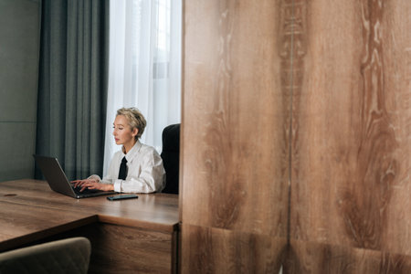 Remote view of focused middle-aged businesswoman sitting at desk typing working on laptop, browse wireless internet. Concentrated elegant senior female employee consult client online using computer.の写真素材