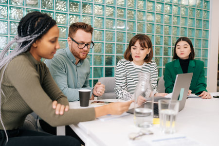 Serious diverse group creative designers cooperating at office conference room sitting desk. Startup...