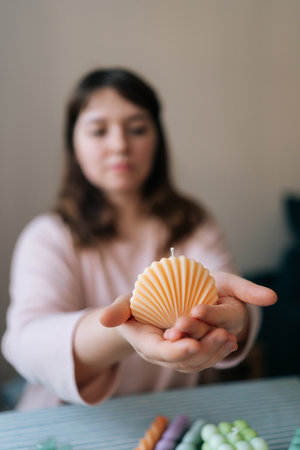 Vertical selective focus shot of female artisan craftperson holding in hand finished candle after create. Process of making handmade scented candle. Creative occupation of making trendy DIY candles.の写真素材