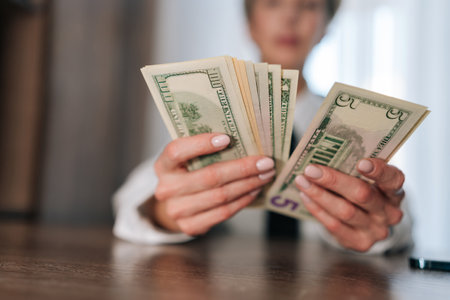 Selective focus of female counting money cash dollars bills one, five, ten, twenty and one hundred dollar banknote sitting at table. Concept of financial accounting budget planning, revenue, wealthの写真素材