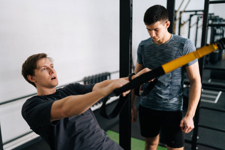 Male using looped ropes doing all-body resistance training. Beginner sportsman doing fitness trx...