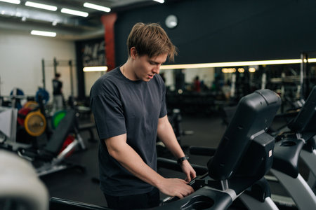 Portrait of athletic man in activewear adjusting settings on treadmill, preparing for cardio session...