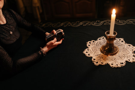High-angle view of unrecognizable enigmatic fortuneteller shuffling deck of tarot cards by light of burning candles. Mysterious wizard performing esoteric rite, forecasting fate. Concept of divinationの写真素材