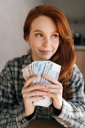 Vertical portrait of happy female freelancer holding in hands wad of Russian rubbles that she earned...