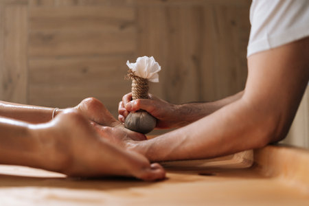 Side view of unrecognizable relaxed young woman getting Ayurvedic feet massage with Kizhi Herbal Bags by male masseur in luxury resort spa salon. Serenity of recreation at wellness centerの写真素材