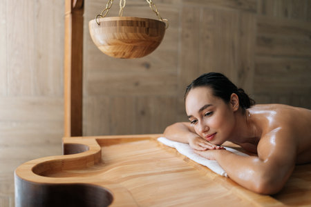 Portrait of tranquil pensive woman lying on massage table with closed eyes enjoying leisure in wellness center. Happy relaxed beautiful female having rest at spa salon. Concept of body careの写真素材