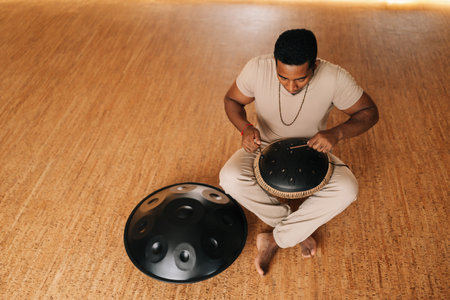 High-angle view of happy African man playing ethnic native music on steel tongue drum with sticks...
