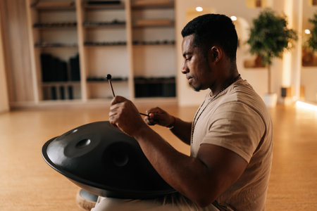 Side view of relaxed African man playing traditional ethnic music on glucophone using sticks sitting on floor in lotus pose. Concept of mindfulness, tranquility, harmony, sound therapy.の写真素材