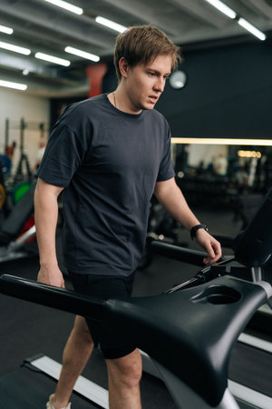 Vertical shot of beginner runner male running on treadmill, finishing exercise and turns off trainer machine. Athletic sportsman resting after intensive cardio workout to burn calories in gym.の写真素材