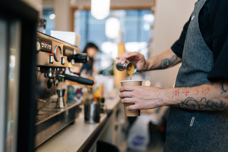 Cropped shot of unrecognizable barista male preparing tasty coffee drink for customer in small business, holding metal pot pouring coffee in espresso shot. Beverage drink for breakfast in cafe.の写真素材