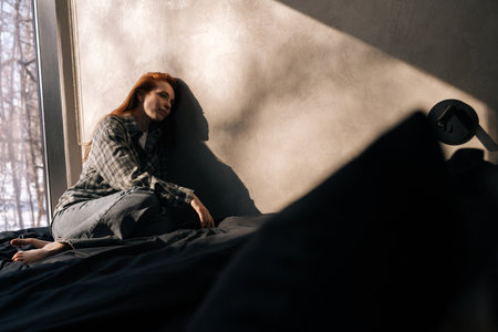 Portrait of sad young woman sitting on floor by window alone feeling depressed looking unhappy, suffers having mental pain, goes through divorce cheated by boyfriend, unwell bad condition.の写真素材