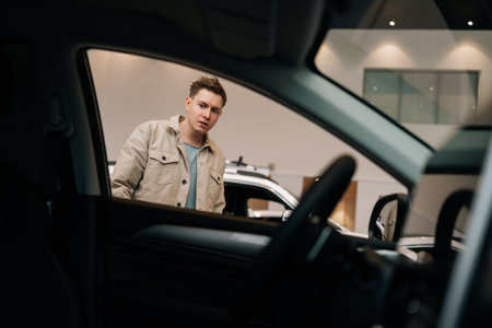 View from car inside to customer male choosing new automobile walking around luxury cars in car...