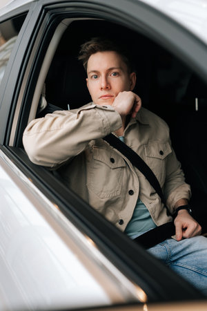Vertical portrait of passenger male sitting on front passenger seat fastening belt harness, looking at camera. Closeup of young man with buckled security belt in car. Concept of safety lifestyle.の写真素材