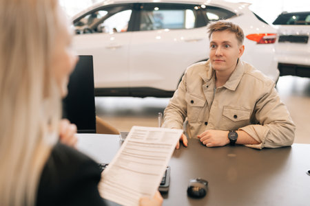 Rear view of unrecognizable female manager giving car purchase documents to male buyer to review and...