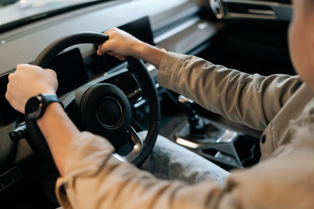 High-angle view cropped shot of male customer sitting behind steering wheel of new car in dealership...