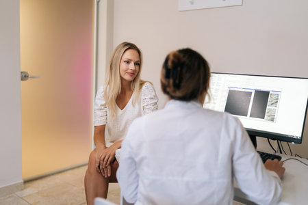 Rear view of unrecognizable female doctor explain to woman patient medical test result sitting at table with computer, giving recommendation about disease treatment medications. Concept of healthcare.の写真素材