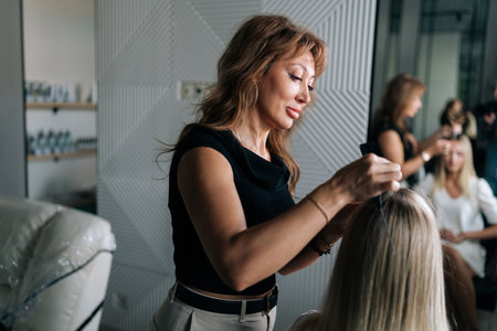 Rear view of female hairstylist applying peeling purifying and soothing cosmetics product to scalp using cotton swabs. Blonde woman client having professional hair beauty treatment.の写真素材