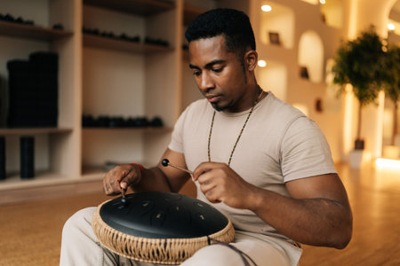 Medium shot of meditate African man in trance enjoying playing ethnic music on glucophone using sticks sitting on floor in lotus pose. Concept of mindfulness, tranquility, harmony, sound therapy.の写真素材