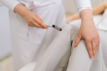Close-up hands of unrecognizable neurologist doctor checking knee reflex of young female patient using hammer. Process neurological physical examination in clinic. Concept of healthcare and medicare.の写真素材