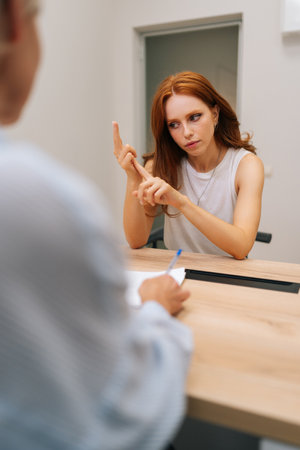 Vertical rear view of troubled woman patient talking to unrecognizable doctor sitting in clinic office, sharing complaints, asking professional specialist about treatment during visit at hospital.の写真素材