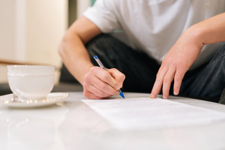 Closeup hands of unrecognizable male client signing papers sitting at table in waiting room. Young...