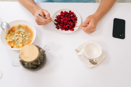 High-angle view of unrecognizable male hospital patient in medical coat resting, eating, gaining strength before long operation in clinic. Man enjoy eating food sitting at table in hospital room.の写真素材
