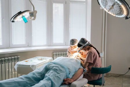 Remote view of two doctors collecting hair follicles from donor area of patient for hair transplantation. Process of hair transplant with FUE Sapphire method in clinic. Concept of baldness treatmentの写真素材
