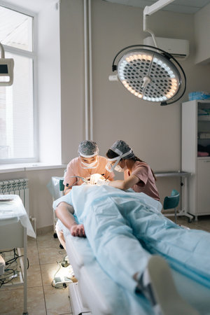Vertical shot of two trichologist specialist collecting hair follicles from donor area of male patient for hair transplantation in clinic. Process of hair transplant with FUE Sapphire method.の写真素材