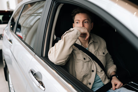 Portrait of thoughtful male customer fastening seat belt sitting on front passenger seat in car....