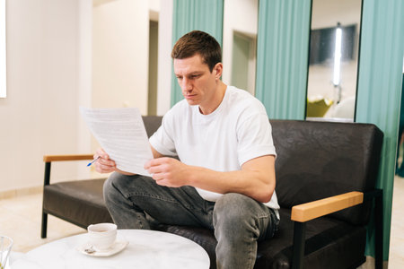 Serious focused male patient in casual clothes reading paper medical contract before signing and...