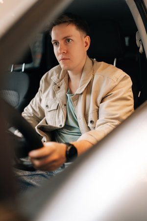 Vertical portrait of handsome customer male sitting in driver seat in new automobile, want buy new...