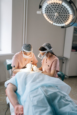 Vertical portrait of two trichologist specialist collecting hair follicles from donor area of male...