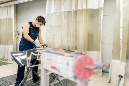 Remote view of professional car service male worker polishing black luxury car hood in auto repair shop using with orbital polisher. Concept of car detailing and polishing.の写真素材