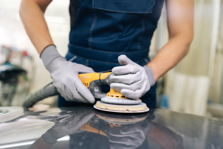Cropped shot of unrecognizable mechanic male in protective gloves polish black hood using grinding unit in automobile repair and renew service station. Concept of automobile maintenance.の写真素材