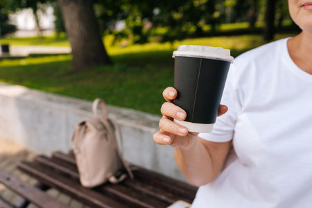 Close-up cropped shot of unrecognizable woman enjoying free time outdoors sipping coffee sitting on bench at city park. Happy female resting alone enjoying summertime. Calm lady drinking tea.の写真素材