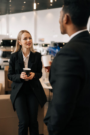 Vertical shot of successful multiethnic business people in formal outfit having break after meeting, talking during drinking coffee together in auto dealership. Concept lifestyle of businesspeople.の写真素材