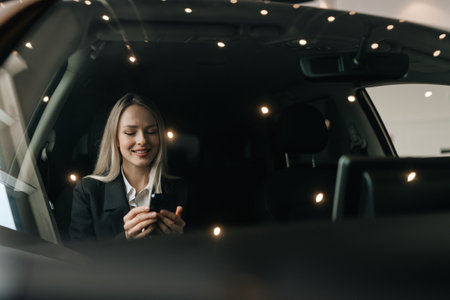 View through windshield to smiling businesswoman in suit reading good news using mobile phone...
