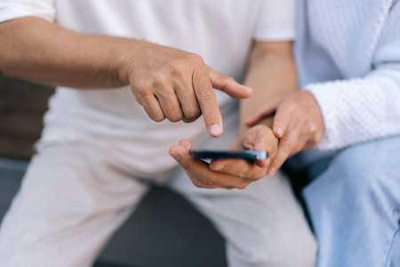 Closeup cropped shot of elderly married couple using smartphone, exploring apps, staying connected with world, embracing digital age in retirement. Senior male and female typing phone together outsideの写真素材