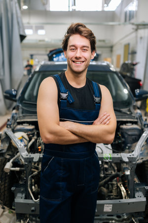 Vertical portrait of positive male car technician wearing uniform smiling looking camera standing posing with crossed hands in auto service shop. Concept of professional automobile maintenance.の写真素材