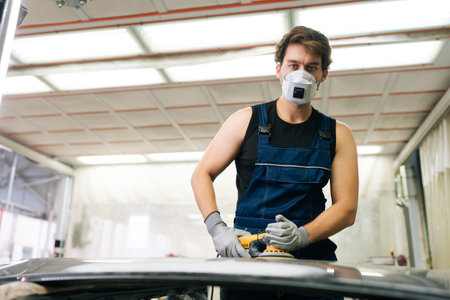 Portrait of skilled mechanic male in face mask polish hood using grinding unit in automobile repair and renew service station. Repair after an accident. Concept of car repair and maintenance work.の写真素材